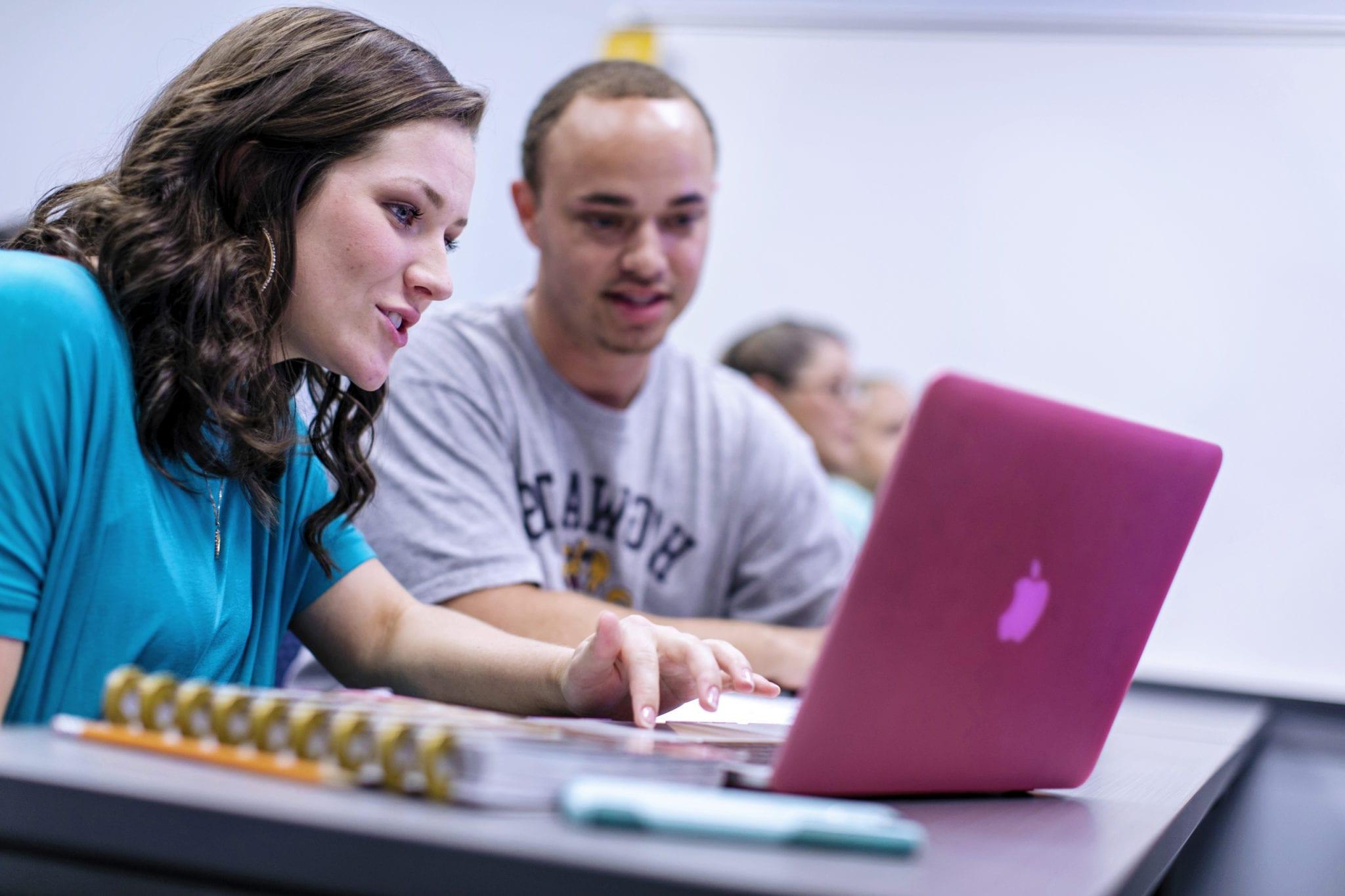 Two students look at a laptop while working in the classroom